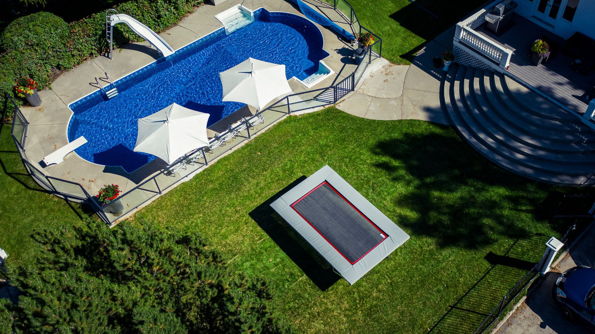 Trampoline and swimming pool with lounge chairs and umbrellas in a backyard setting