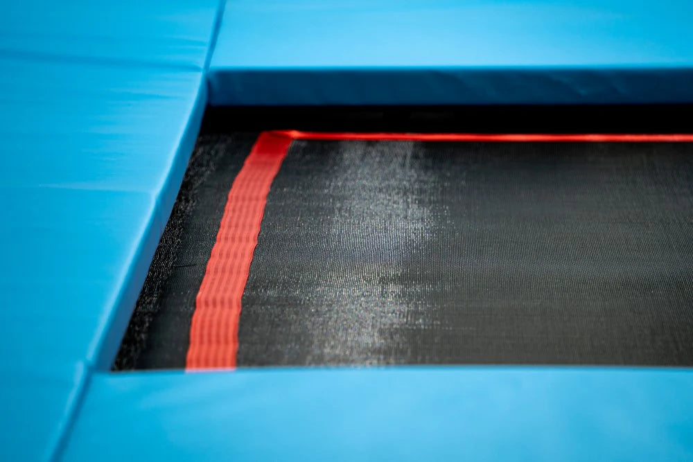 Close-up of a blue trampoline with a red safety strap on a black surface.