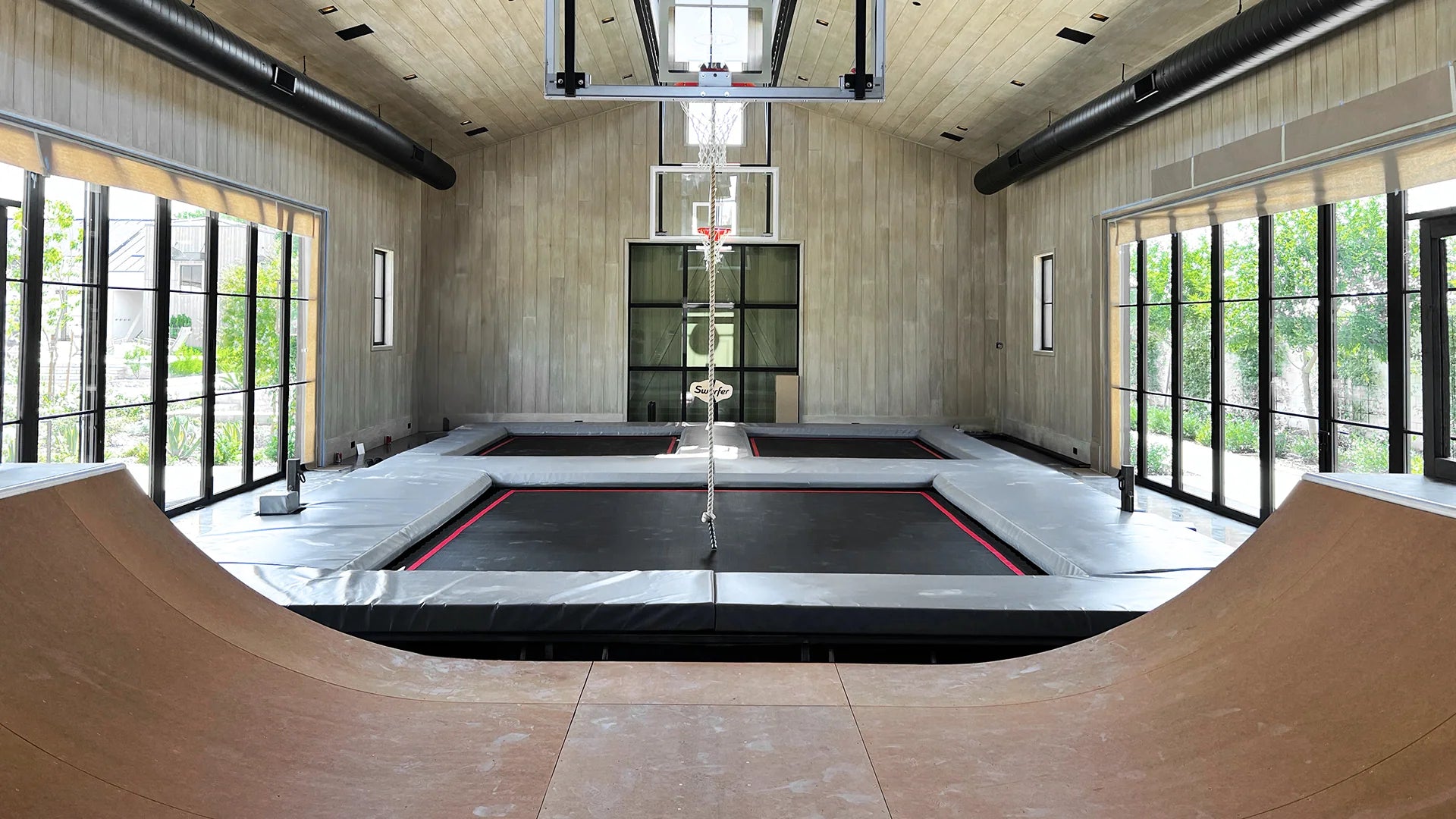 Indoor skate park trampoline room with ramps and basketball hoop.