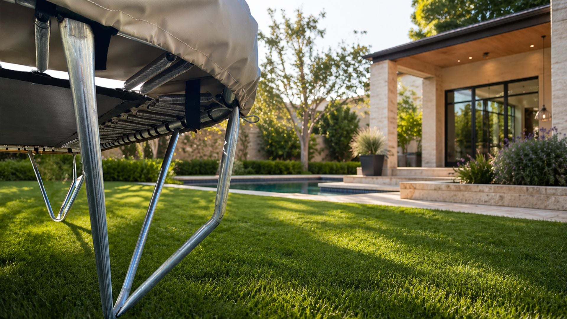 Trampoline on a grassy lawn with a pool and house in the background